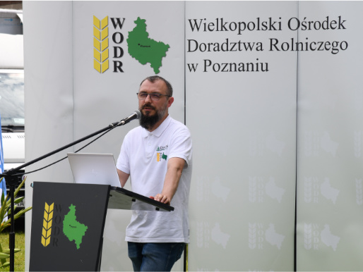 Mężczyzna w średnim wieku - Maciej Zacharczuk - stoi i przemawia przez mikrofon przy mównicy. W tle widać logo WODR.