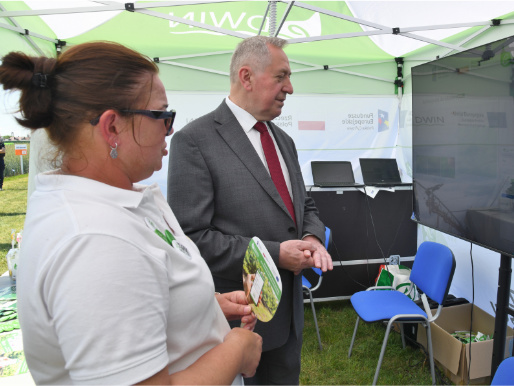 Minister rolnictwa Henryk Kowalczuk rozmawia z kobietą w średnim wieku, doradczynią WODR, na stoisku platformy eDWIN oraz spogląda na ekran telewizora na którym wyświetlone są dane dotyczące eDWIN.